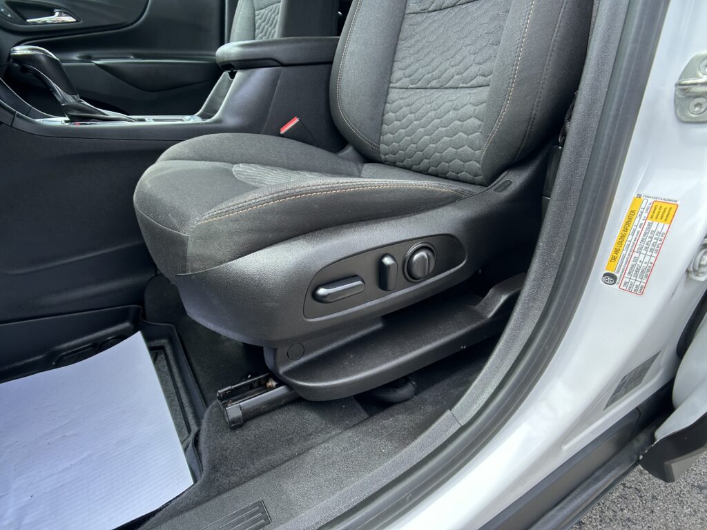 Front seat area of a car interior with textured dark fabric seat, orange stitching, center console, and red seat belt buckle visible at the side of the seat station.