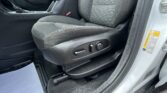 Front seat area of a car interior with textured dark fabric seat, orange stitching, center console, and red seat belt buckle visible at the side of the seat station.