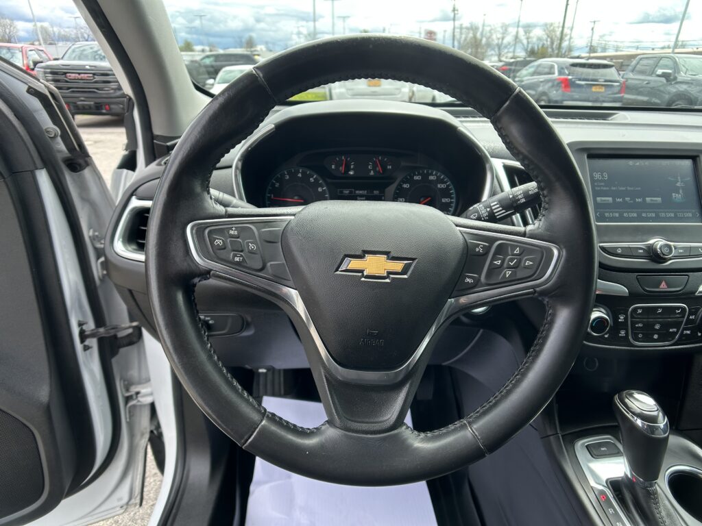 View from the driver's seat: steering wheel with Chevrolet emblem, instrument cluster, and center console, with a parking lot visible through the windshield.