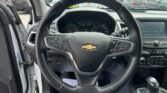 View from the driver's seat: steering wheel with Chevrolet emblem, instrument cluster, and center console, with a parking lot visible through the windshield.