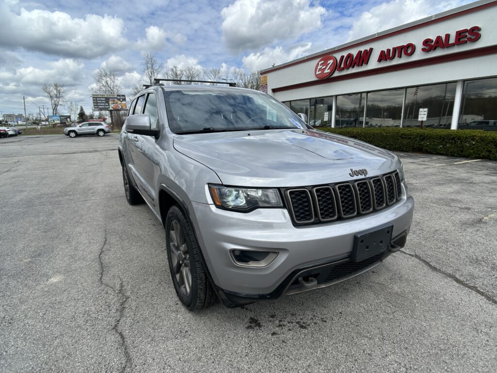 Silver Jeep SUV parked in a lot in front of an EZ Loan Auto Sales storefront with a large red sign and glass windows under a cloudy sky