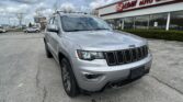 Silver Jeep SUV parked in a lot in front of an EZ Loan Auto Sales storefront with a large red sign and glass windows under a cloudy sky