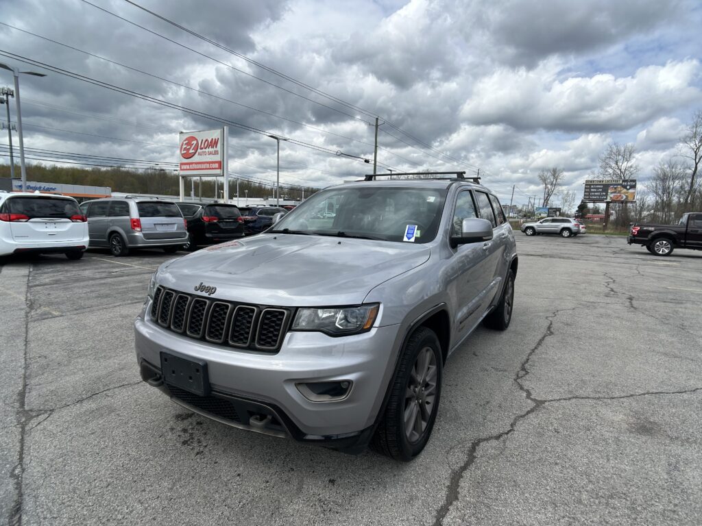 Silver Jeep SUV in the foreground of a busy car dealership lot with a prominent E-Z LOAN Auto Sales sign and cloudy sky above.