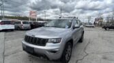 Silver Jeep SUV in the foreground of a busy car dealership lot with a prominent E-Z LOAN Auto Sales sign and cloudy sky above.