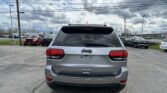 Rear view of a silver Jeep SUV in a parking lot with other cars and a cloudy sky above.