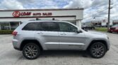 Silver SUV (Grand Cherokee) parked in front of EZ Loan Auto Sales with a blue-sky backdrop and dealership signage above the building rim.
