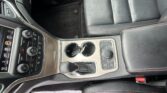 Interior of a car showing the center console with gear selector, two cup holders, and black leather seats with red stitching