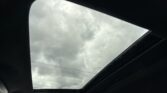 Inside a car looking up through an open glass sunroof at a gray cloudy sky