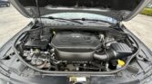 Open car hood revealing engine compartment; black V6 engine cover with various hoses and components visible in the bay.