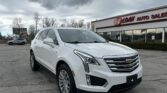 White Cadillac SUV parked in a dealership lot in front of an EZ Loan Auto Sales building with cloudy sky above.