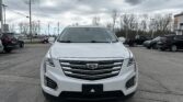 Front view of a white Cadillac SUV parked in a lot with a cloudy, overcast sky above.
