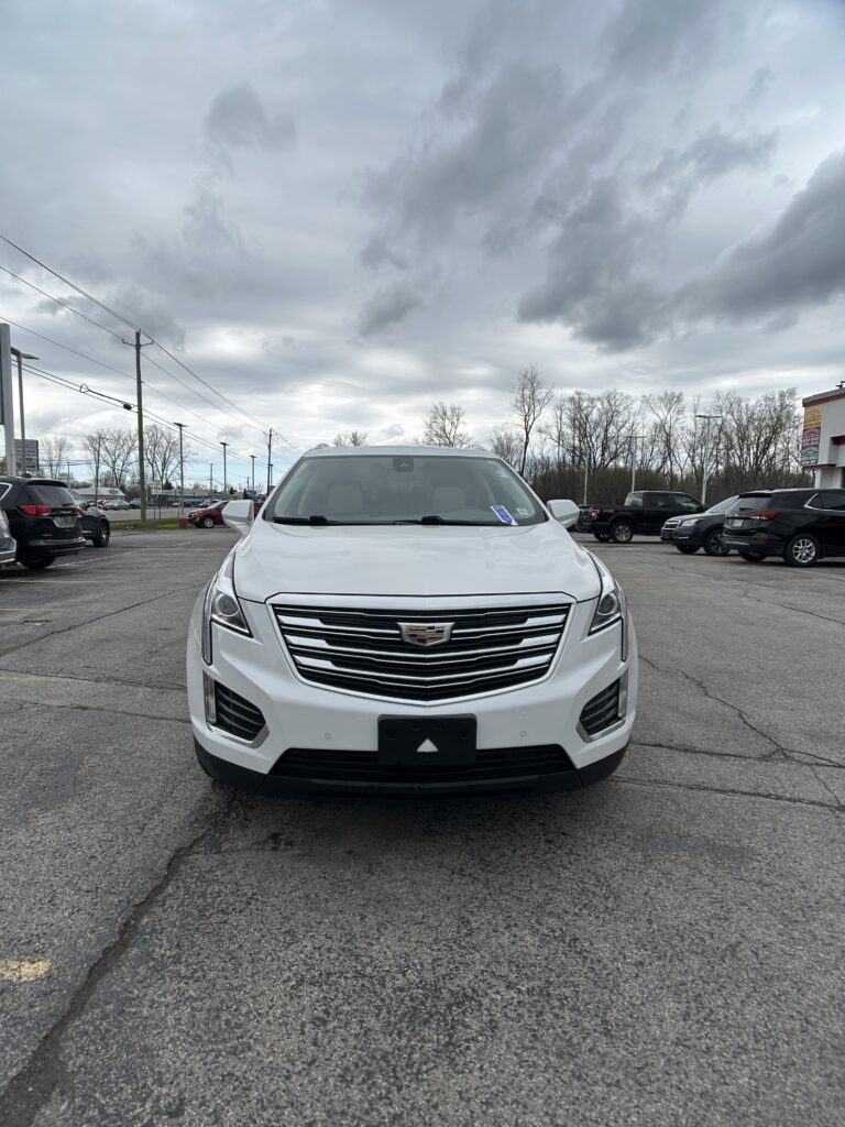 Front view of a white Cadillac SUV parked in a lot with a cloudy, overcast sky above.