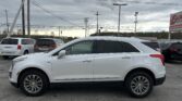 White SUV in a dealership parking lot with other cars, under a cloudy sky and power lines overhead