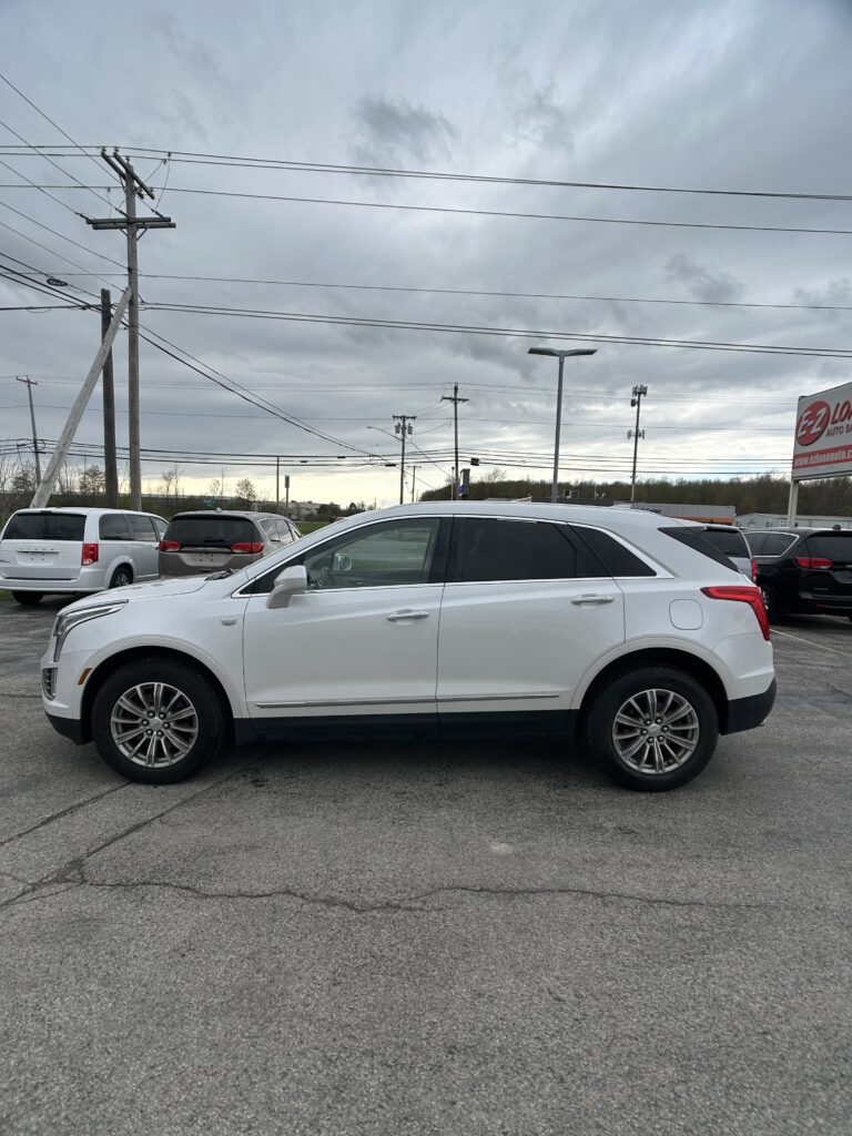 White SUV in a dealership parking lot with other cars, under a cloudy sky and power lines overhead