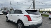 Rear three-quarter view of a white Cadillac XT5 SUV parked in a lot with a cloudy sky and utility poles in the background.