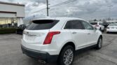 White Cadillac SUV parked in a dealership lot under an overcast sky, with power lines overhead and other cars in the background