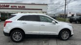 White SUV parked in a dealership lot with 'LOAN AUTO SALES' signage and cloudy sky in the background.