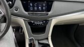 Interior of a modern car showing the center touchscreen, push‑start, gear lever, and cup holders with a parking lot outside the windshield.