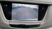 In-car rearview camera display showing a parking lot with orange guide lines over the pavement and surrounding parked cars.