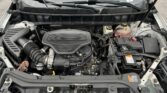 Front engine bay with hood open, showing a V6 engine, battery, and coolant reservoir in a Cadillac SUV/truck head-on view at the grille area.