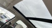 Interior of a car with beige leather seats and a large panoramic sunroof; overhead console with controls visible.