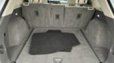Open SUV trunk with beige interior, showing folded third-row seats and a spacious cargo area with floor mats stacked on the floor.