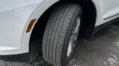 Front left wheel of a white SUV with visible tire tread, wheel well, and a fender badge on the door
