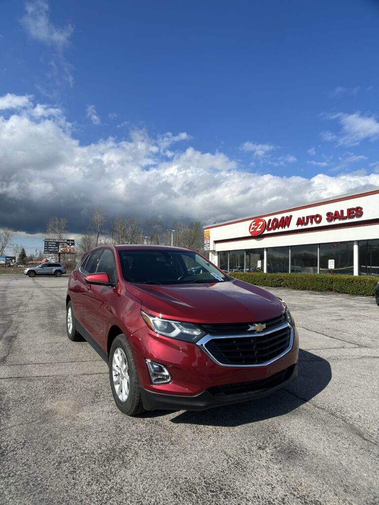Red Chevrolet SUV in a dealership lot with EZ Loan Auto Sales building in the background and a blue sky above.