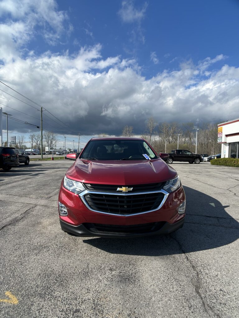 Red Chevrolet SUV photographed from the front in a parking lot with a cloudy sky overhead.