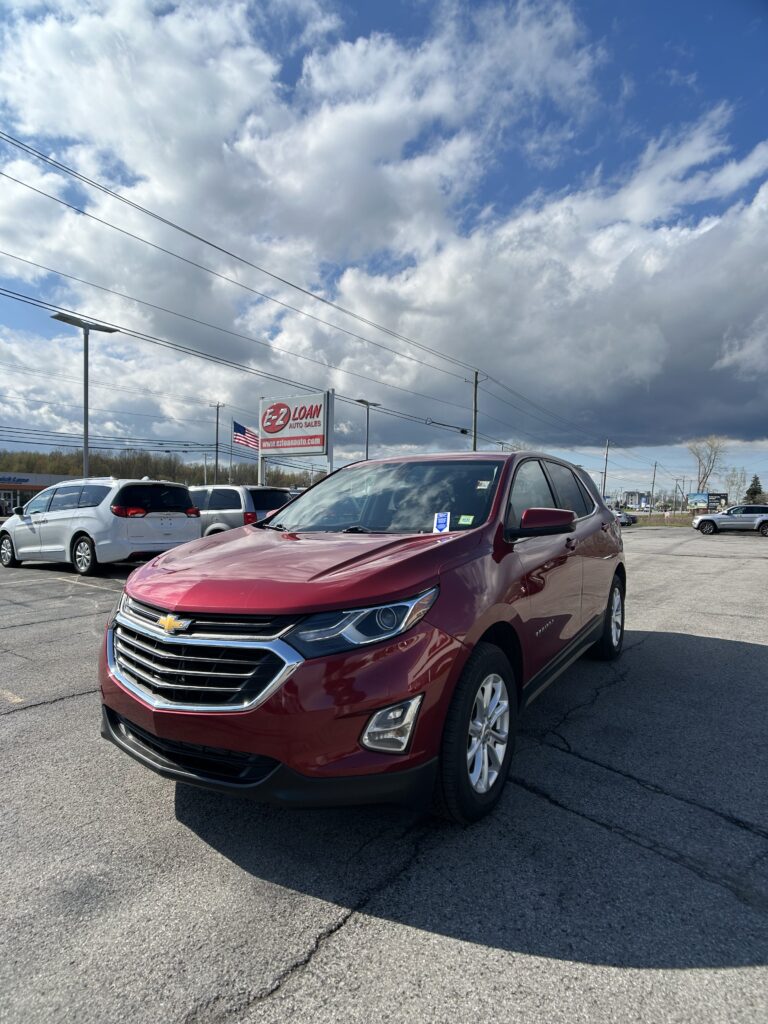 Red Chevrolet SUV in a car dealership lot with EZ Loan Auto Sales sign and other vehicles under a cloudy sky.