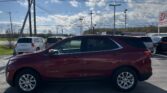 Red Chevrolet Equinox SUV parked in a lot with utility poles and overhead power lines under a bright blue sky with scattered clouds in the background.