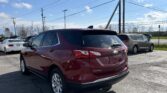 Rear three-quarter view of a red Chevrolet Equinox parked in a dealership lot with power lines overhead and a blue sky.