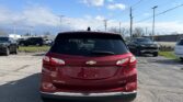 Rear view of a red Chevrolet Equinox AWD LT in a parking lot, with other vehicles and power lines overhead against a blue sky.