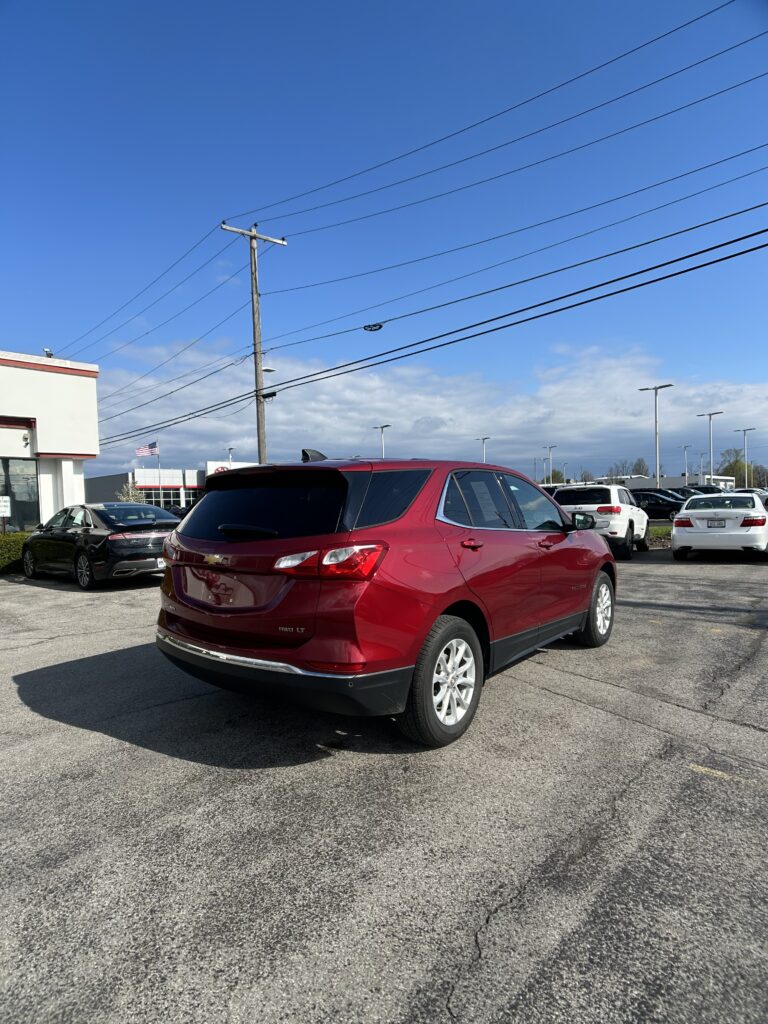 Red SUV parked in a dealership lot with other cars and a blue sky above, power lines crossing the scene.