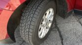 Close-up of a red car wheel and tire, showing the front fender and the photographer's reflection in the glossy paint.
