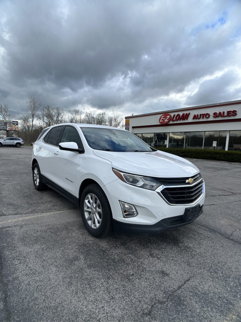 White Chevrolet Equinox parked in a car lot in front of EZ Loan Auto Sales on a cloudy day with a red sign on the building signage visible