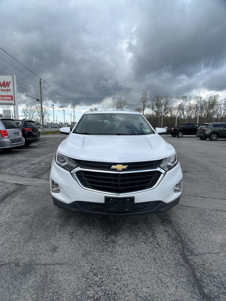 Front view of a white Chevrolet SUV parked in a lot with dark stormy clouds overhead.