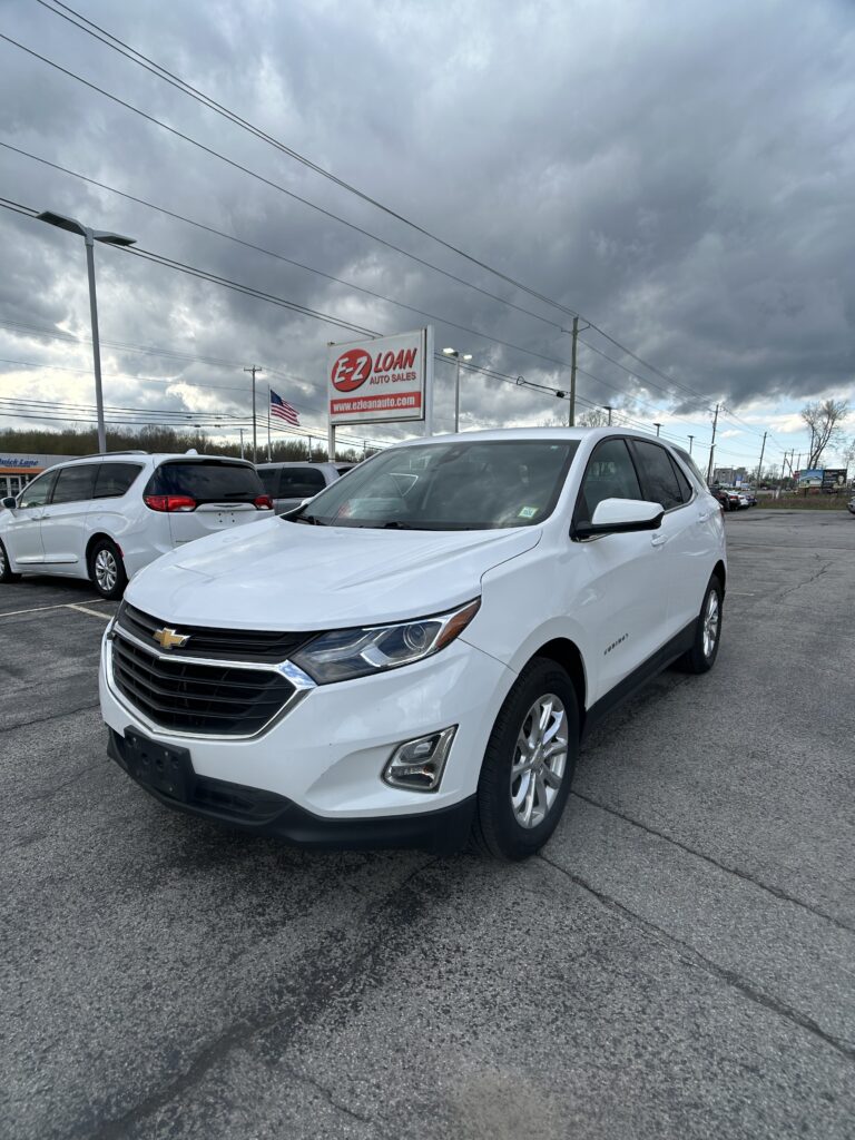 White Chevrolet SUV parked in a dealership lot with an EZ Loan Auto Sales sign and a cloudy sky in the background.