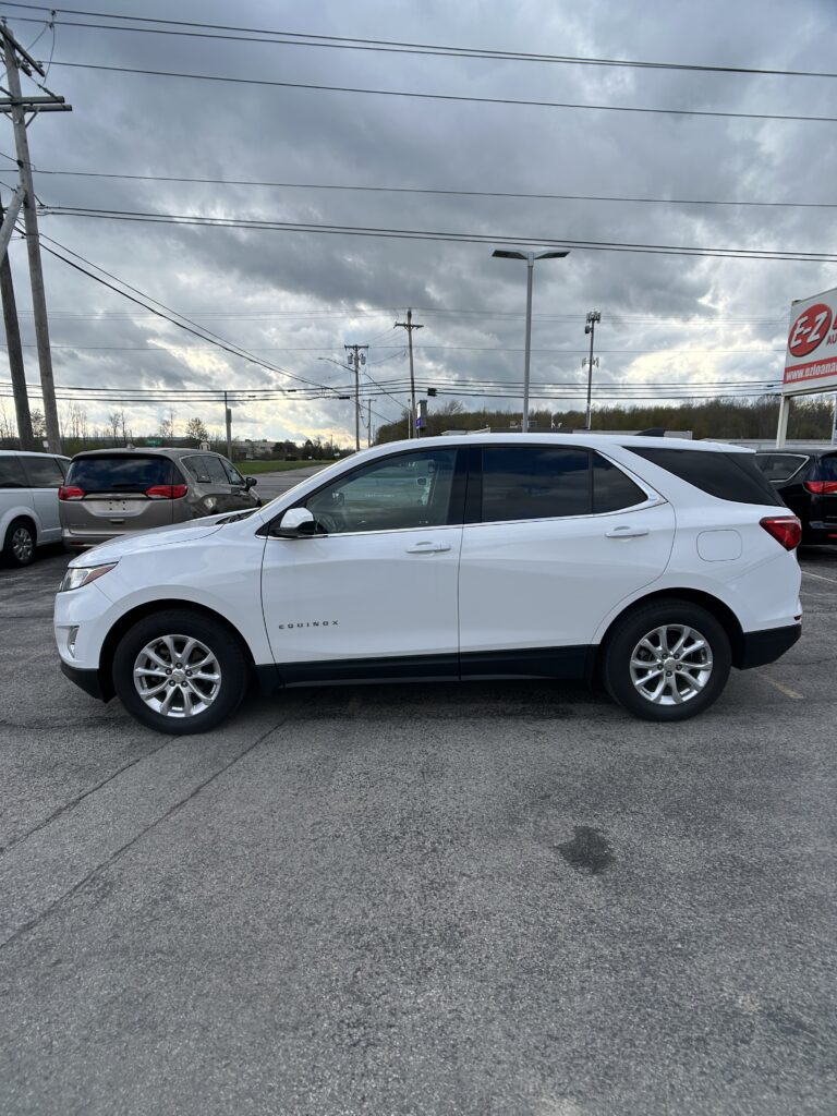 White Chevrolet Equinox SUV parked in a lot, shown in profile under a cloudy sky with power lines overhead.