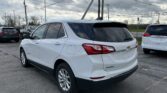 White Chevrolet Equinox parked in a lot, with tall utility poles and overhead power lines against a cloudy sky.