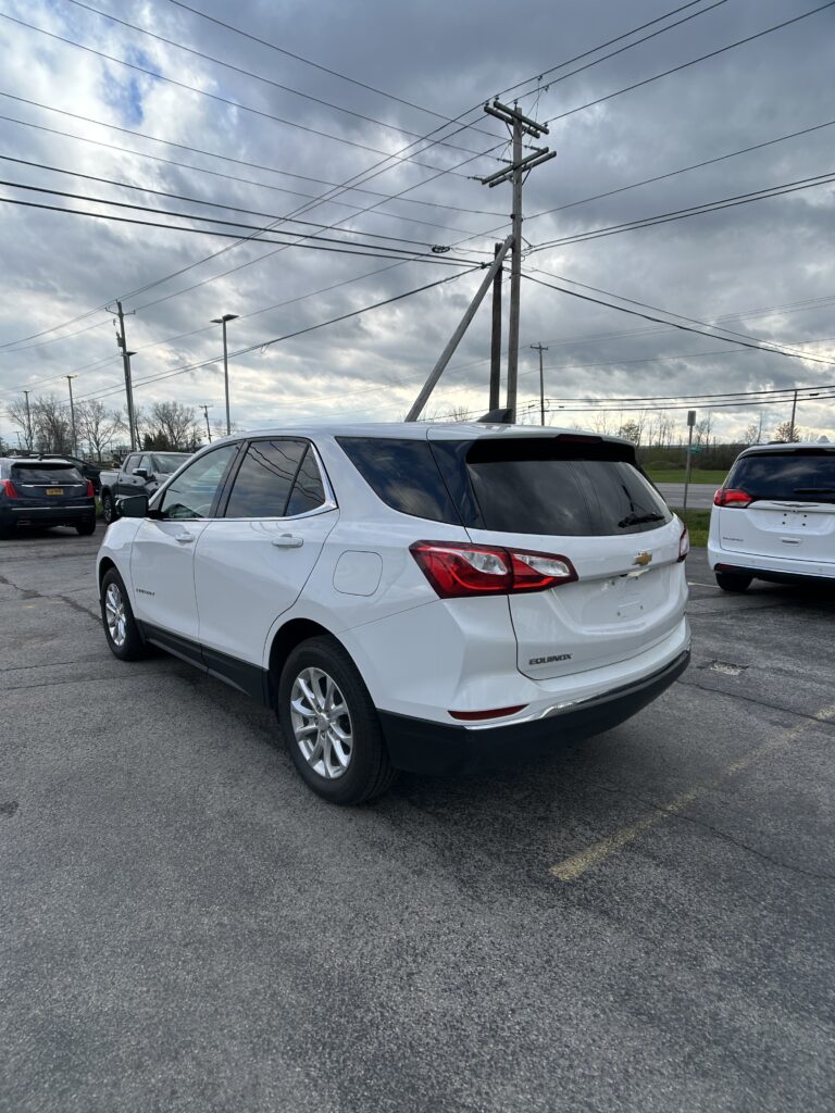 White Chevrolet Equinox parked in a lot, with tall utility poles and overhead power lines against a cloudy sky.