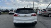 Rear view of a white Chevrolet Equinox LT in a parking lot, with other cars and power lines overhead against a cloudy sky.