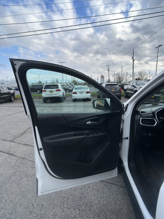Open front passenger door of a white car in a dealership parking lot; black interior visible.