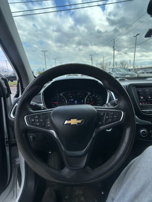 Close-up of car interior from the driver’s seat showing the steering wheel with Chevrolet logo and the dashboard, with a cloudy sky through the windshield.