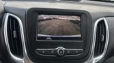 Car dashboard interior with a central touchscreen showing the rear-view parking camera in a parking lot scenario