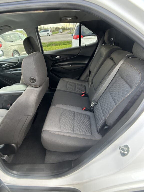 Back seat area of a car showing quilted gray upholstery, headrests, and three seat belts in a dark interior.
