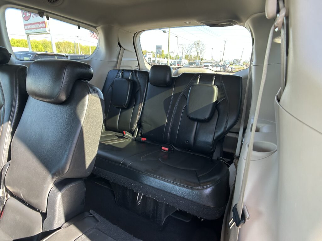 View of the back row in a SUV with black leather seats, headrests, and visible seat belts; outside street traffic seen through the windows.