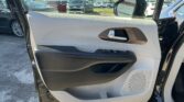 Open car door interior with beige and black trim, window controls, and a view of a parking lot full of cars outside.