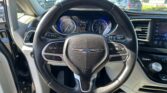 Driver's perspective of a car cockpit with steering wheel and digital instrument cluster visible, dashboard and infotainment screen on the right, outside parking lot visible through windshield