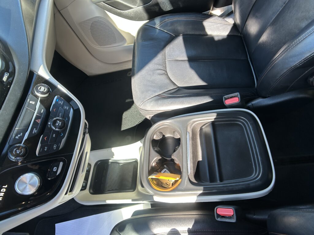 Front passenger seat and center console in a black leather car interior, cup holder visible by the seat belt buckle.